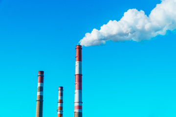 Smoking pipes of the plant against the blue sky, white smoke from the pipes