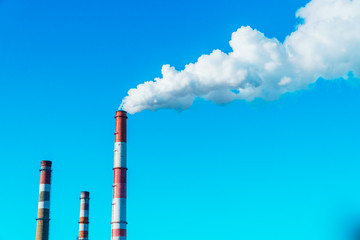 Smoking pipes of the plant against the blue sky, white smoke from the pipes