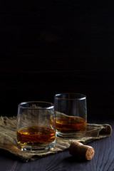 alcoholic drinks. glass of whiskey with ice on a black background. two glasses of whiskey on a wooden table with burlap and cork.