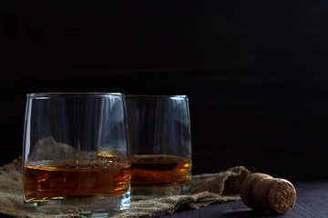 alcoholic drinks. glass of whiskey with ice on a black background. two glasses of whiskey on a wooden table with burlap and cork. horizontal orientation