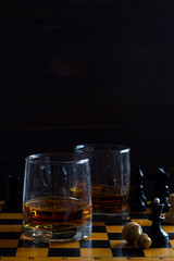 alcoholic drinks. glass of whiskey with a chess queen and pawn on a black background. two glasses of whiskey on a chessboard with chess pieces. vertical orientation