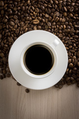 mug with black coffee on a saucer and on a wooden background with coffee beans with place for text