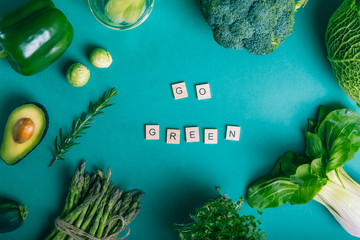 Top view healthy raw vegetables frame on the green background with Go Green message on wooden blocks. Vegetarian and vegan diet. Veganism concept. Sustainable lifestyle, good, real plant-based foods.