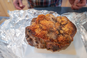 Crispy crackling on the top of roasted pork shoulder just out of the oven. Home cooked in a kithcen. A man can be seen near by. Shallow focus on the front edge of the crackling