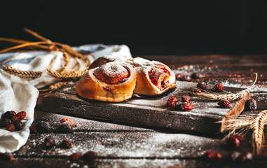 Sweet pastry removed from the oven with strawberry jam and pressed with sugar powder on an old wooden background with wheat ears and  hip rose .