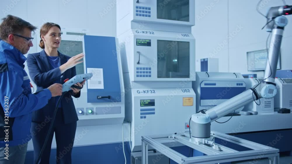 Fototapete Modern Factory: Female Project Manager and Male Engineer Standing, Talking and Using Tablet Computer for Programming Robot Arm Assembly Line. Industry 4.0 Facility with High Tech CNC Machinery