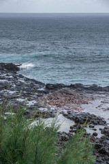 Koloa, Kauai, Hawaii, USA. - January 16, 2020: Gray-azure Pacific Ocean with black rocky coastline shows spot of the Spouting Horn geiser. Inactive at this moment, located in the brown rock. Some gree