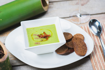 Green vegetarian broccoli cream soup with rye crackers on a wooden table in a restaurant or cafe.