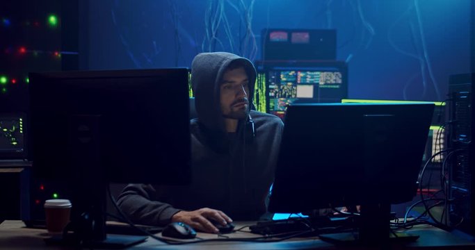 Caucasian young man sitting and working at the computer in the dark room with technologies, hacking the system and laundring data.