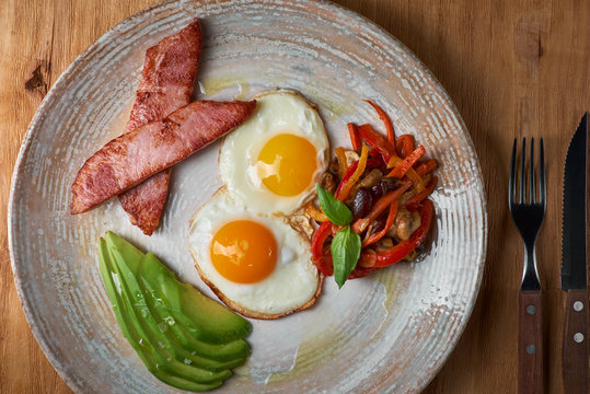 plate of fried eggs with bacon and avocad on wooden table. English breakfast on table