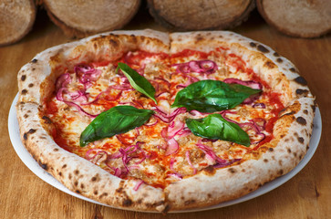 Italian Pizza with tuna and red onion on a wooden board in a rustic kitchen or pizzeria on an old wooden table