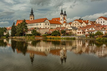 Fototapeta na wymiar Telc / Czech Republic - September 27 2019: View of the castle, the tower of the church of James the Great and historical houses over a lake. Reflection of the cityscape and dramatic blue sky in water.