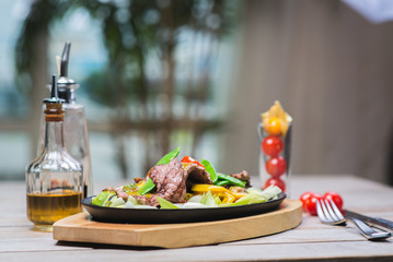 Fried pieces of meat with vegetables in a hot pan on a wooden table in a restaurant.