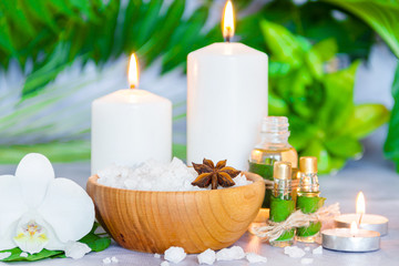 Fototapeta na wymiar Small glass bottles with aromatic massage oils, wooden bowl of salt, burning candles, green plants are on table. Ayurveda salon concept. Preparation for spa and relax healing treatments.