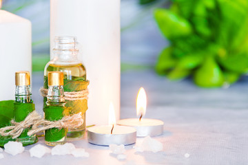 Obraz na płótnie Canvas Closeup small glass bottles with aromatic massage oils, burning candles, green plants, salt are on table. Ayurveda salon concept. Preparation for spa and relax healing treatments, therapy.