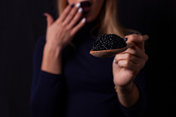 Beautiful Fashion Model woman eating black caviar. Beauty girl portrait with caviar on her lips. Fashion female with spoon of black Caviar isolated on Black background