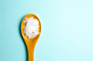 Magnesium Chloride Flakes scattered around brown wooden spoon on blue background. For making foot bath, taking a magnesium-rich bath allows full body exposure to a concentrated solution of magnesium. - obrazy, fototapety, plakaty
