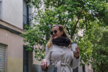 Fototapeta premium Beautiful caucasian blonde woman smiles while having coffee in the street after shopping