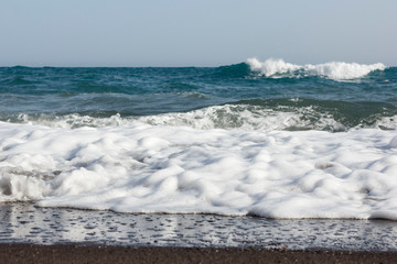beaches with black volcanic sand and soft volcanic pebbles, with waves of white sea foam on the island of Santorini in Greece