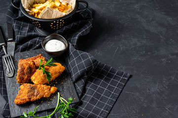 Fish and chips, French fries and cod fillet fried in breadcrumbs. Black background. Top view. Copy...