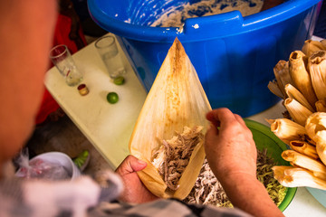 A person cooking a traditional Mexican tamal made of corn flour and meat with sauce
