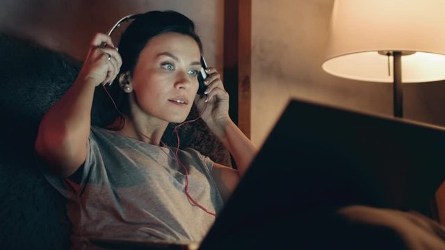 Woman starts watching movie on laptop. Brunette listening music on headphones.