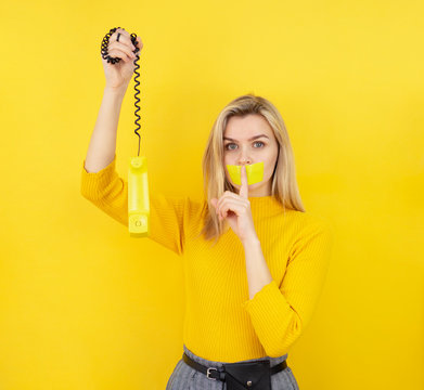 A woman talking on the wiretapped phone on a yellow background with a quieter gesture. Tracking and Spying Warning concept. Don't talk