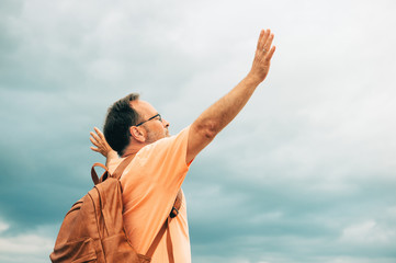Man standing on the top of the hill, wearing backpack, arms wide open