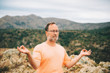 Outdoor portrait of handsome middle age man meditating, relaxing in the top of the mountain