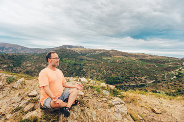 Naklejka premium Outdoor portrait of handsome middle age man meditating, relaxing in the top of the mountain