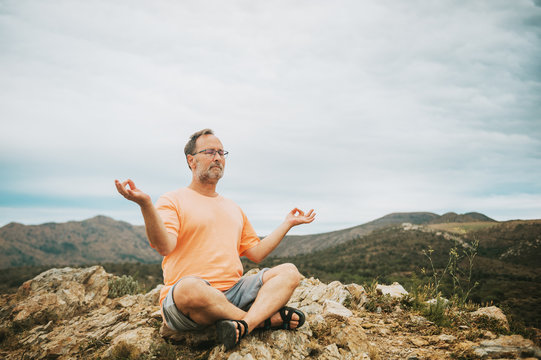 Outdoor portrait of handsome middle age man meditating, relaxing in the top of the mountain