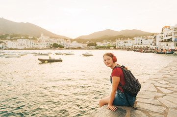 Fototapeta na wymiar Outdoor portrait of happy teenage girl relaxing by the sea, wearing backpack and sunglasses