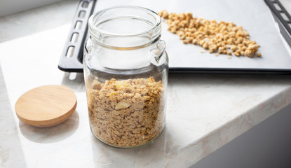 Muesli in glass jar on marble kitchen table. Made homemade granola, healthy breakfast concept. Toned photo