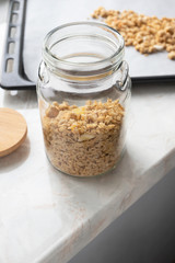 Close-up muesli in glass jar on parchment paper on baking sheet, above. Made homemade granola, healthy breakfast concept