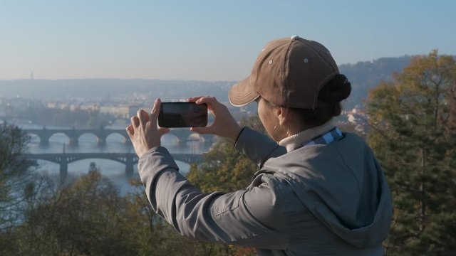 Take a photo of Prague bridges. A woman photographs the old Prague bridges from the observation deck.