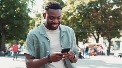 Handsome african-american young man using phone walk on street smile sunlight sunset cellphone fashion internet face outside technology black city mobile summer happy - Powered by Adobe