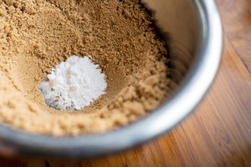Brown sugar in a silver bowl with baking powder on a  wooden kitchen bench