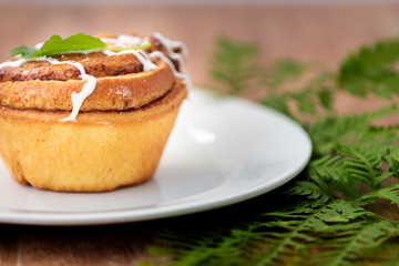 Small cake drizzled with white icing and garnished with a leaf on a white plate resting on a green fern decoration