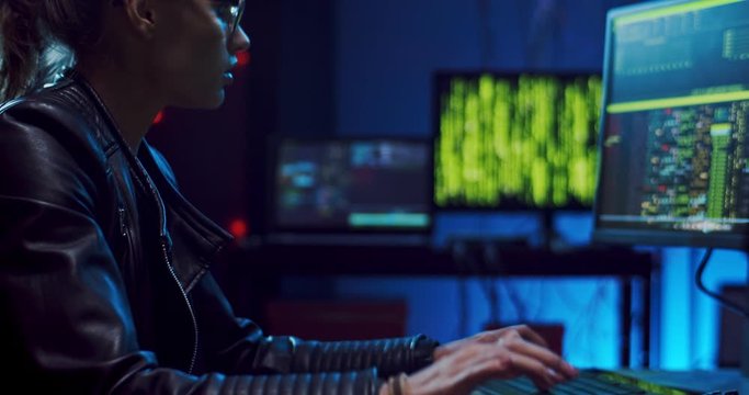 Close up of the Caucasian young female hacker or software developer in glasses tapping, typing and texting on the keyboard of computer at night while programming and coding.