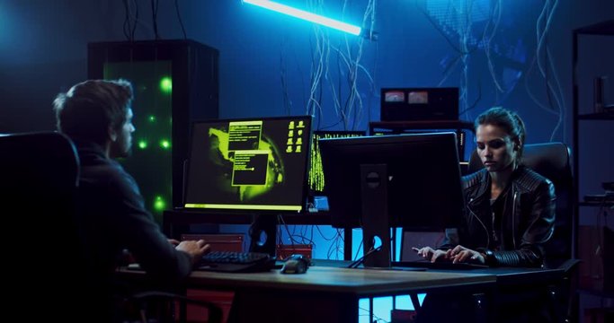 Couple of Caucasian software developers, man and woman sitting at the computers and working at night at creating website or antivirus program.