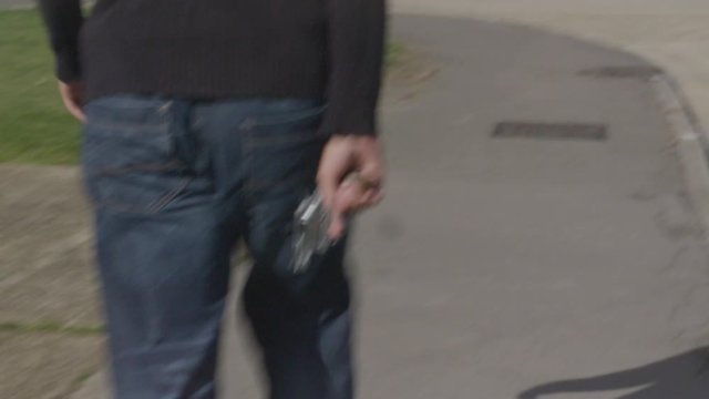 Handheld shot walking behind a man hiding a revolver behind his back