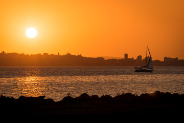 hills and city behind a sailboat on the sunset