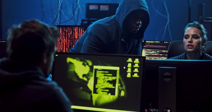 Multiethnic young hackers, men abd woman sitting in the dark room at night at the computers while working with software programs.
