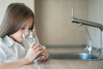 A glass of clean mineral water in kids hands. Little caucasian girl holding a glass. Concept of environment protection. Lifestyle, losing weight, perfect health, care
