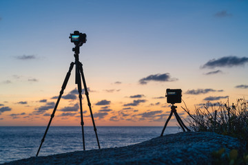 Two cameras standing on a tripods on the beach against the background of dawn