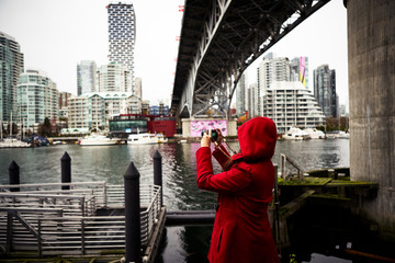 Young Woman in Red Hooded Coat taking picture of scenery in Vancouver's False Creek Water Inlet on a Rainy Day 