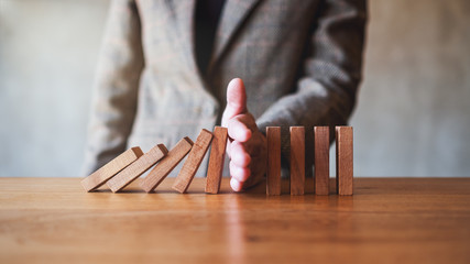 Closeup image of a businessman's hand try to stopping falling wooden dominoes blocks for business...