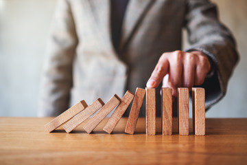 Closeup image of a businesswoman's finger try to stopping falling wooden dominoes blocks for...