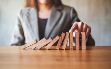 Closeup image of a businesswoman's finger try to stopping falling wooden dominoes blocks for...