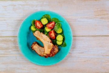 Pork spareribs with BBQ sauce and fresh salad on blue plate.